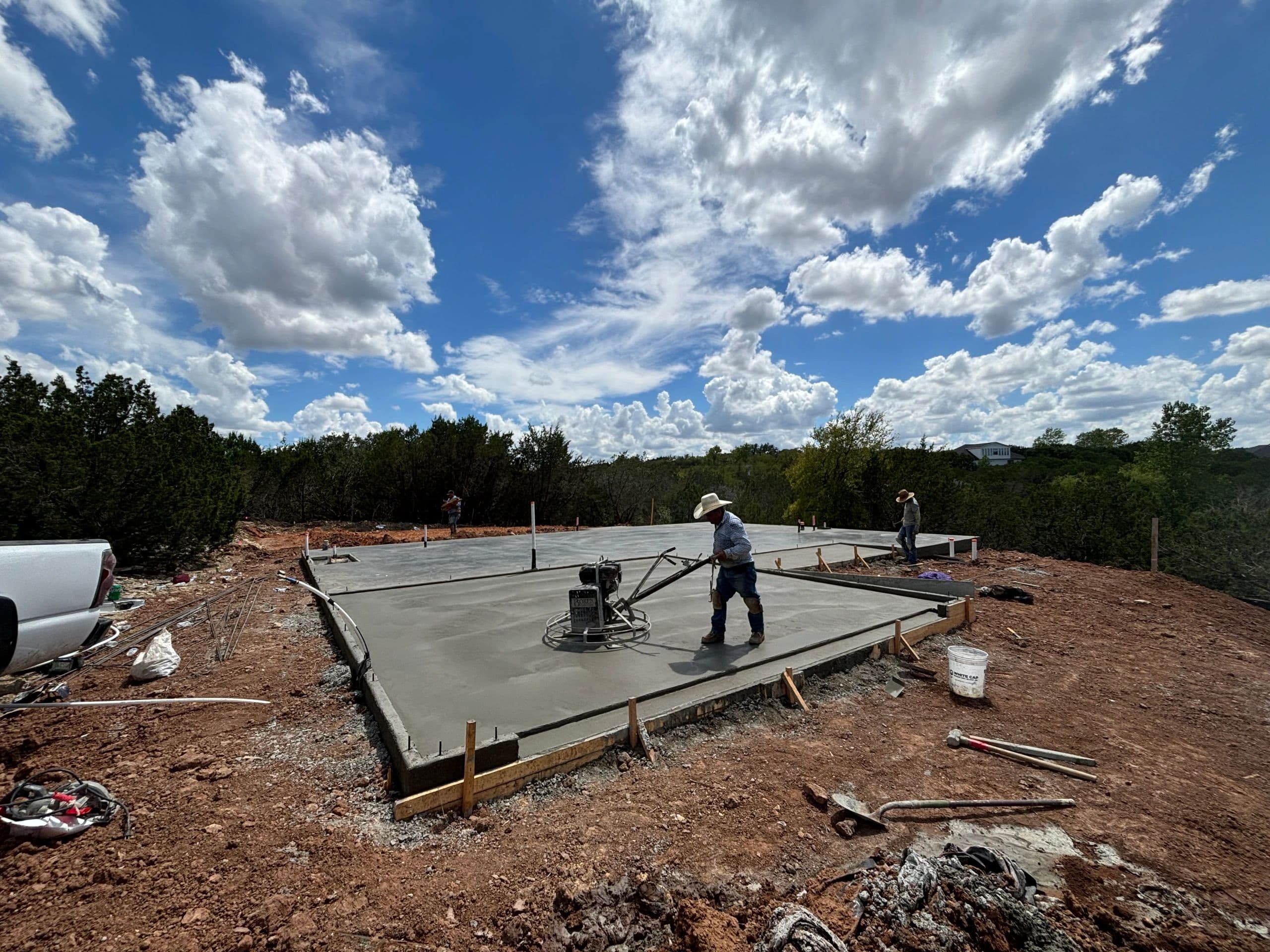 Crew finishing concrete slab with power trowel under Texas sky